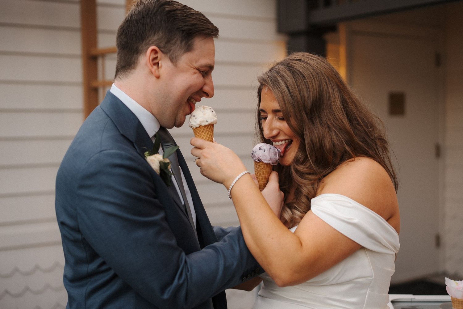 A couple shares a joyful candid moment together outside a white building on their wedding day.