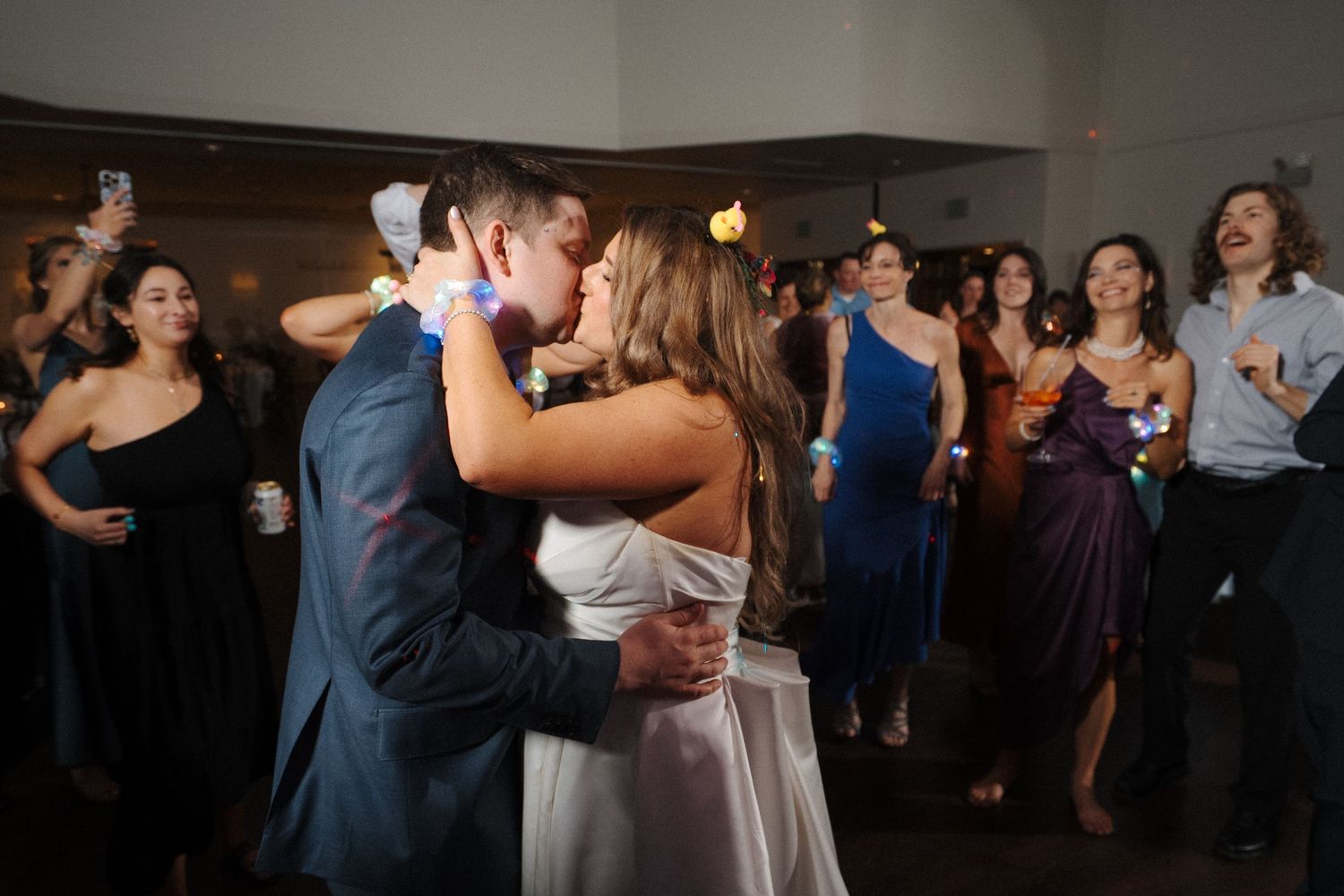 A romantic first dance at a wedding reception with guests watching in formal attire in the background.