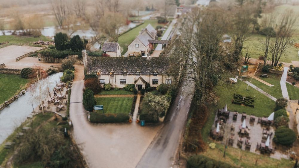 Aerial view of a historic stone building with landscaped gardens and winding pathways in a rural countryside setting.