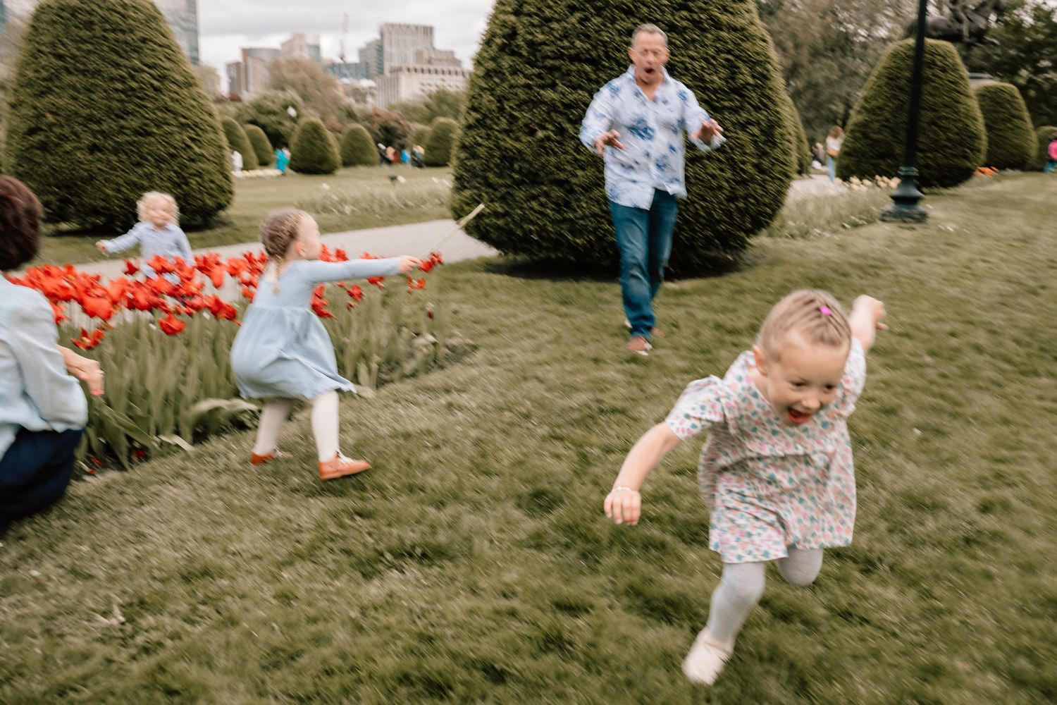 Children running and playing in a garden with colorful tulips while someone chases after them on a grassy hill.