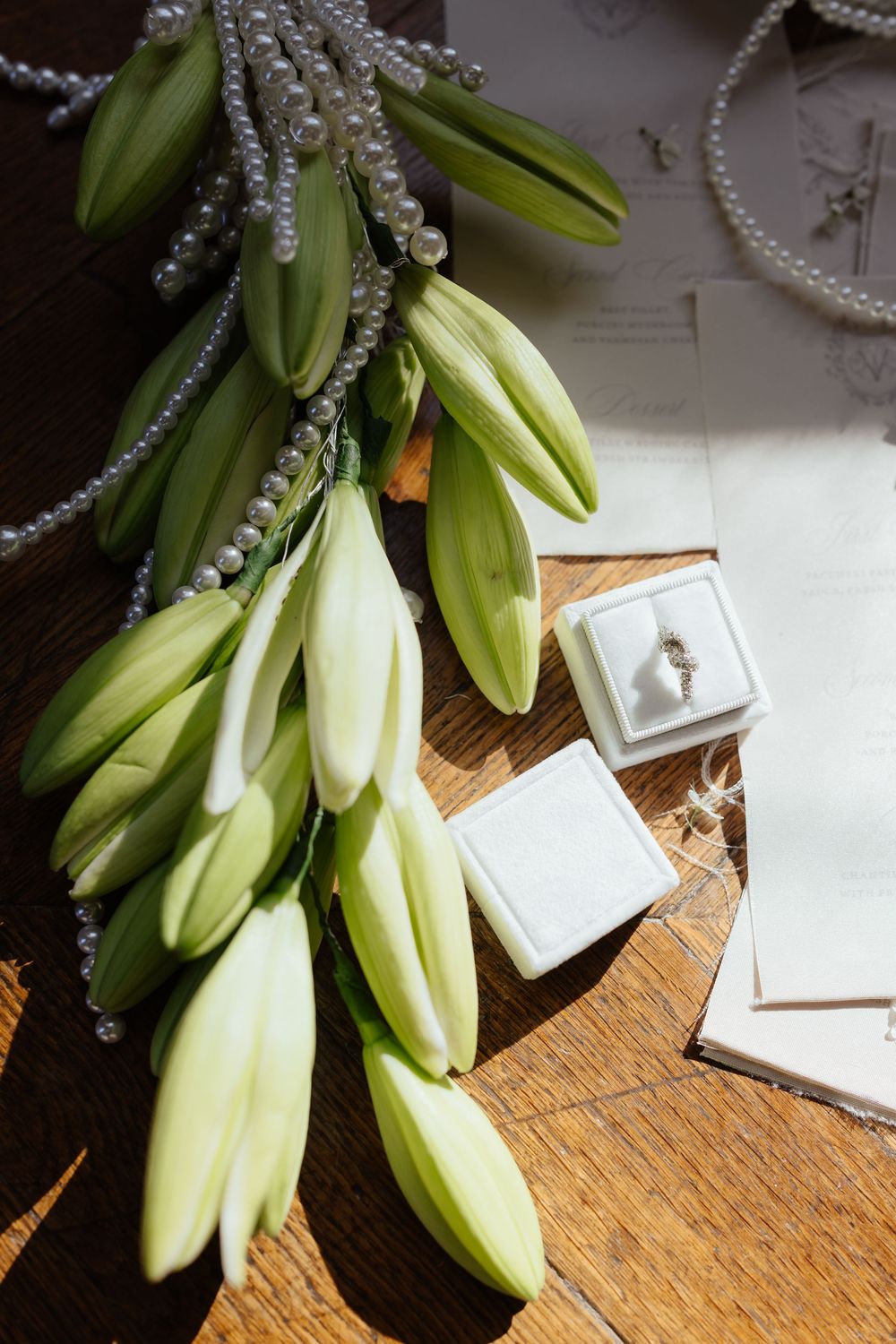White lily flowers and pearl decorations arranged on wooden surface with small ring box.