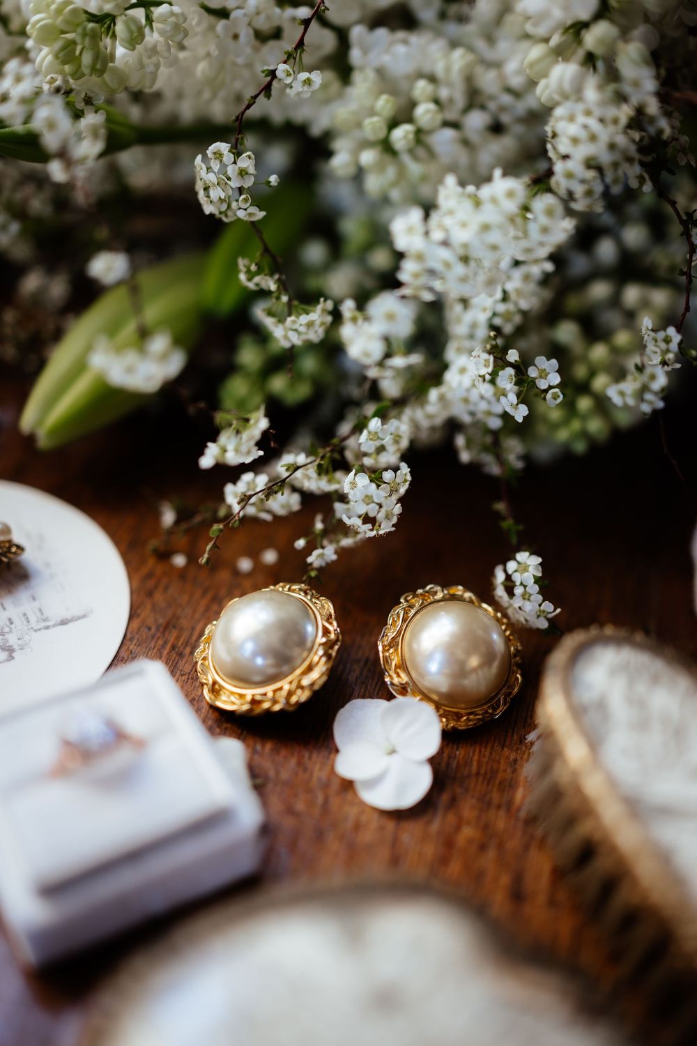 Elegant pearl and gold earrings displayed with delicate white flowers on a wooden surface.