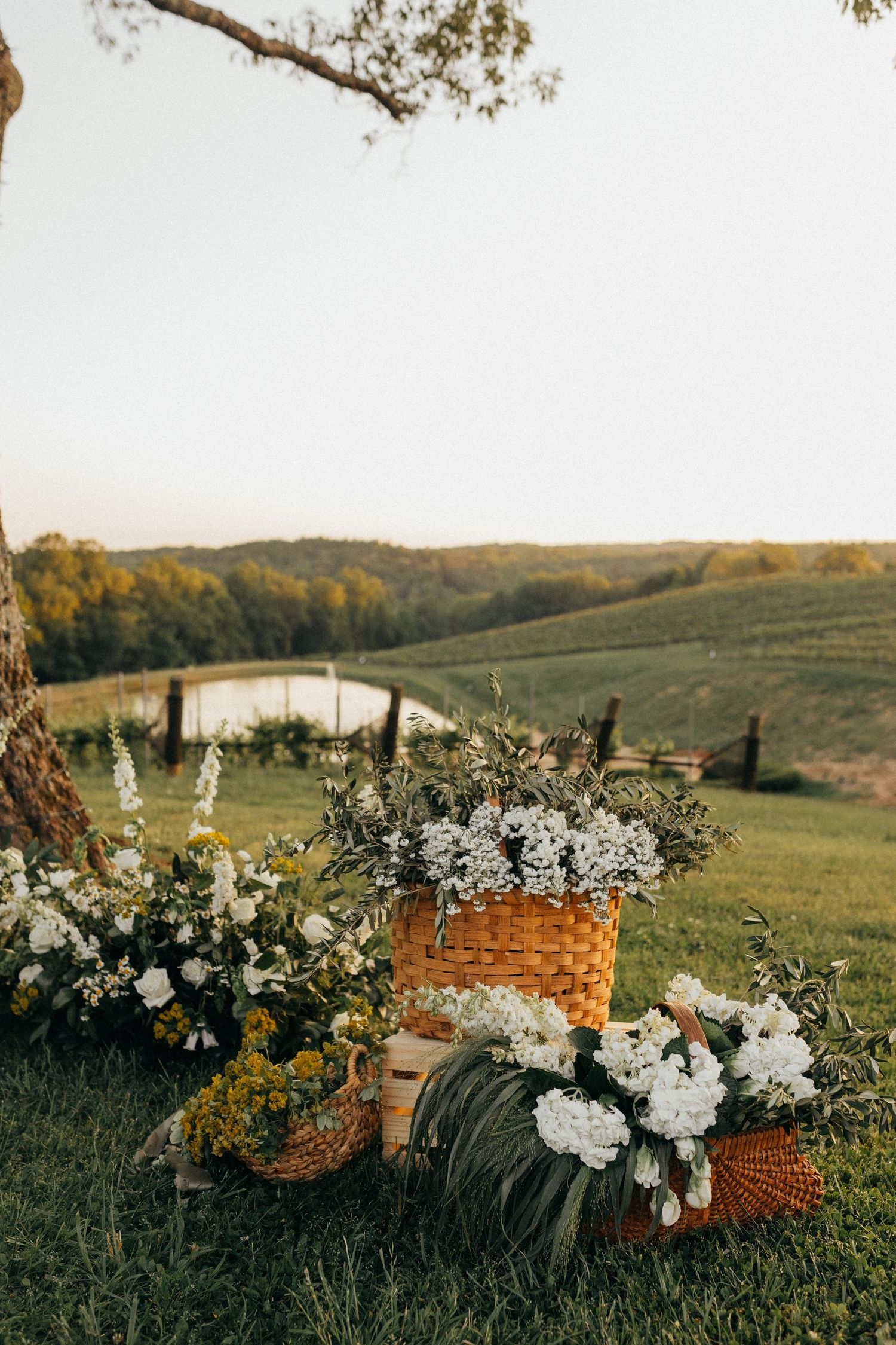 A rustic wicker basket filled with white wildflowers and baby's breath sits on a grassy hillside during golden hour.
