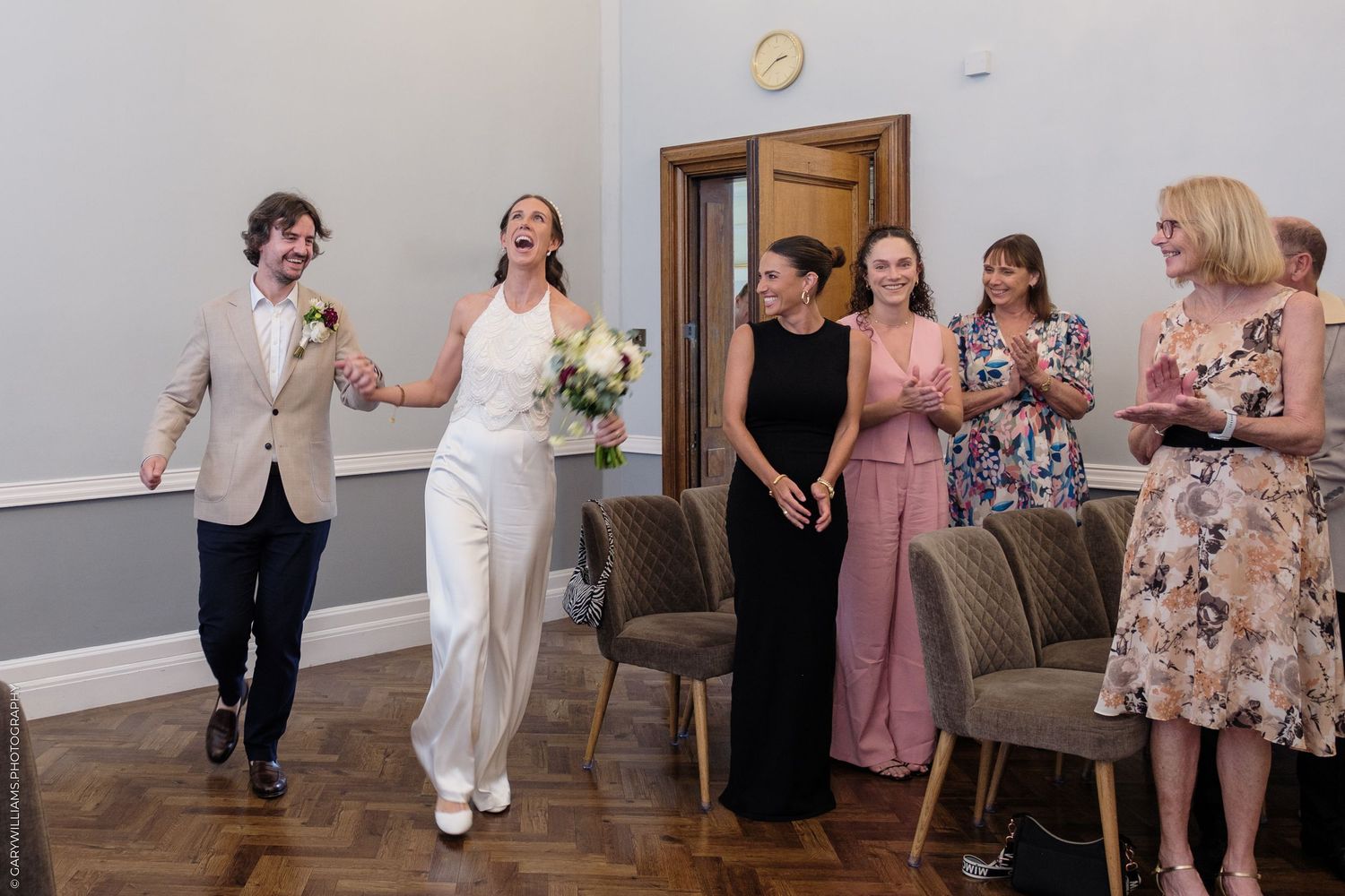 Wedding guests celebrate during reception with drinks and laughter in a modern event space with hardwood floors and gray walls.