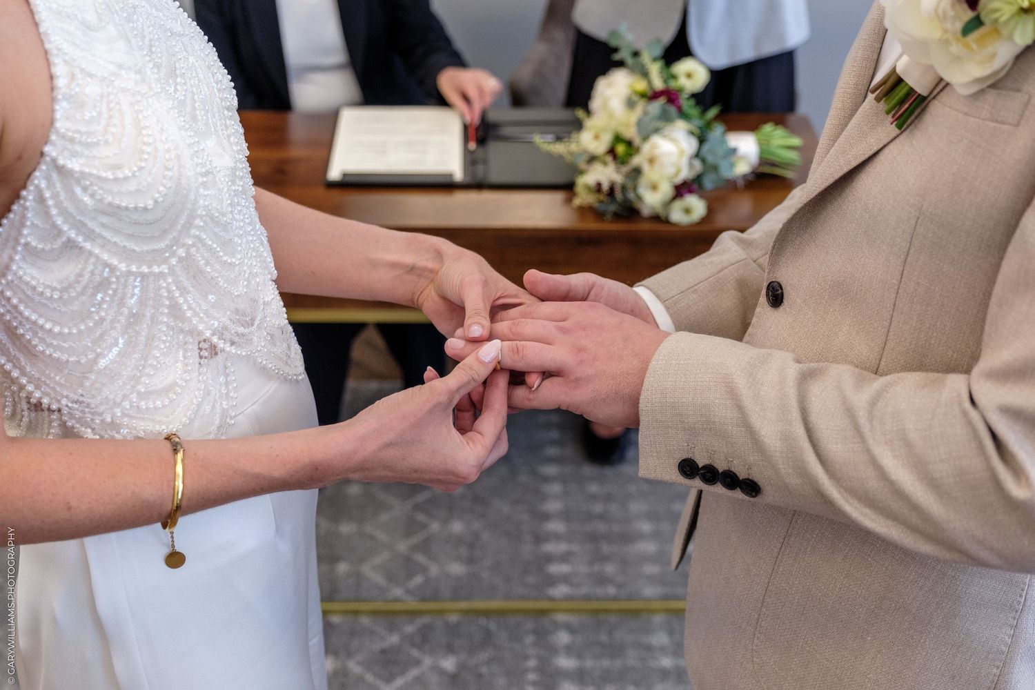 A close-up of hands during a wedding ceremony as a ring is being exchanged between two people.