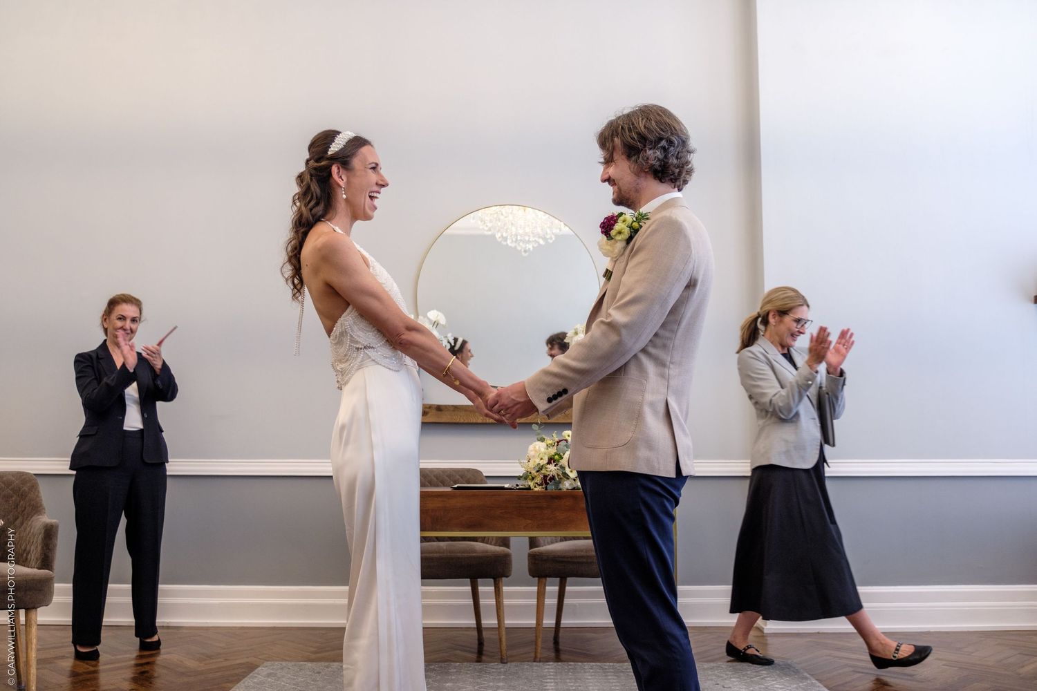 A couple performs a romantic first dance together during a wedding celebration in a sunlit room with white walls.