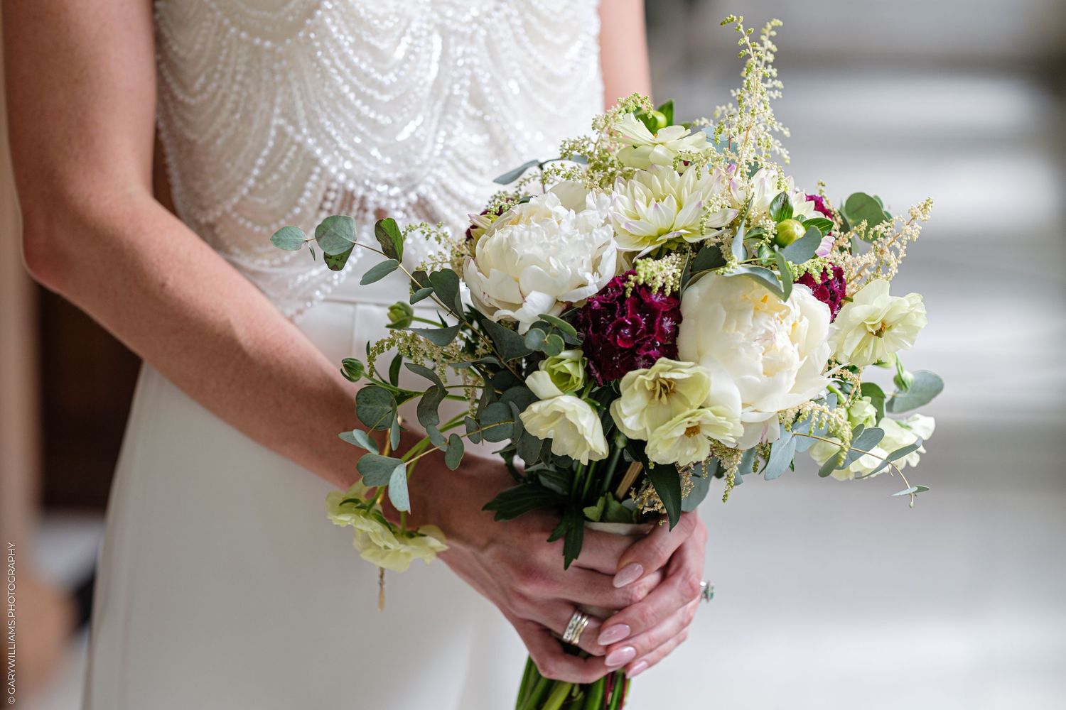 A lovely bridal bouquet featuring white peonies, burgundy accents and delicate eucalyptus greenery.