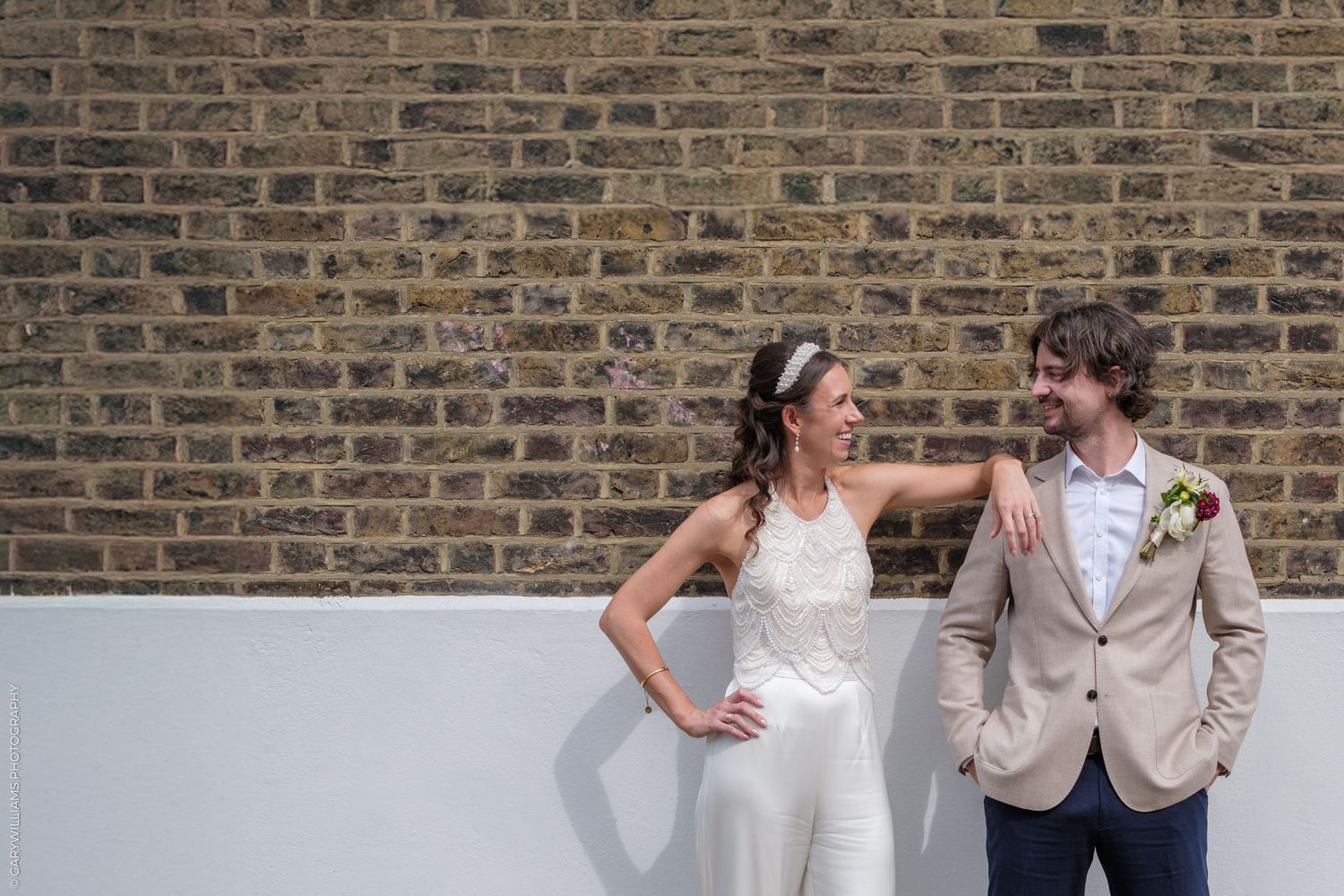 A bride and groom share candid moments together in front of a rustic brick wall during their wedding photo session.