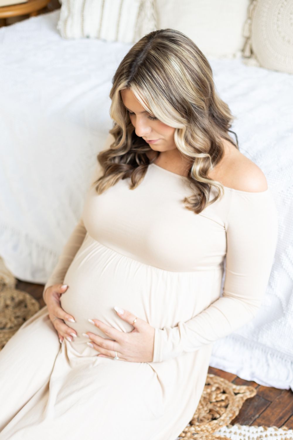 Expectant mother in cream dress sits on floor for intimate maternity portrait.