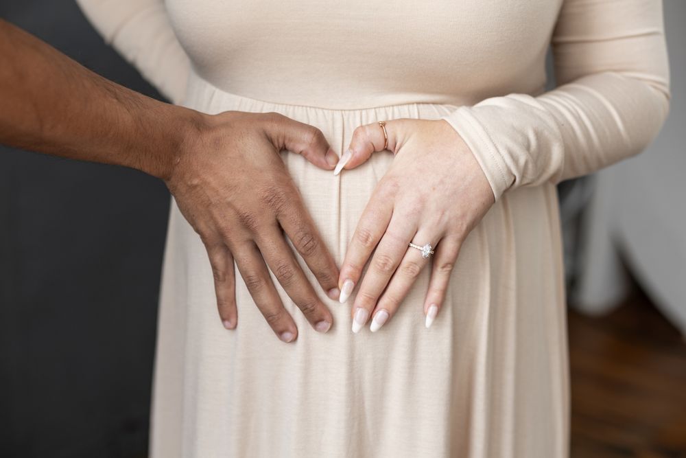 Close-up of hands forming heart shape on pregnant belly in cream dress.