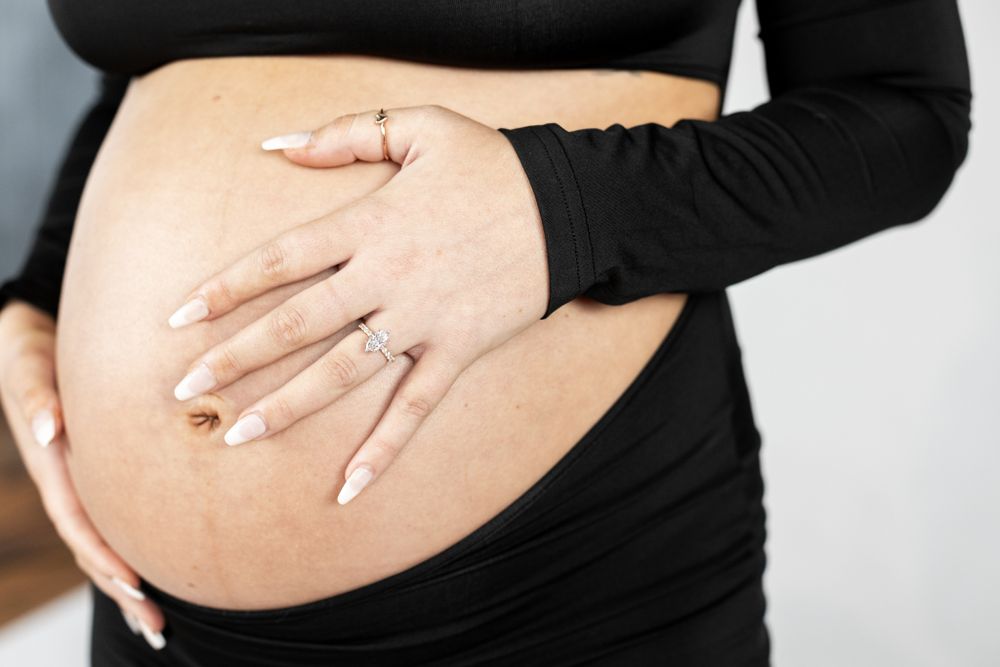 Close up of hands cradling a pregnant belly while wearing a black long sleeve top.