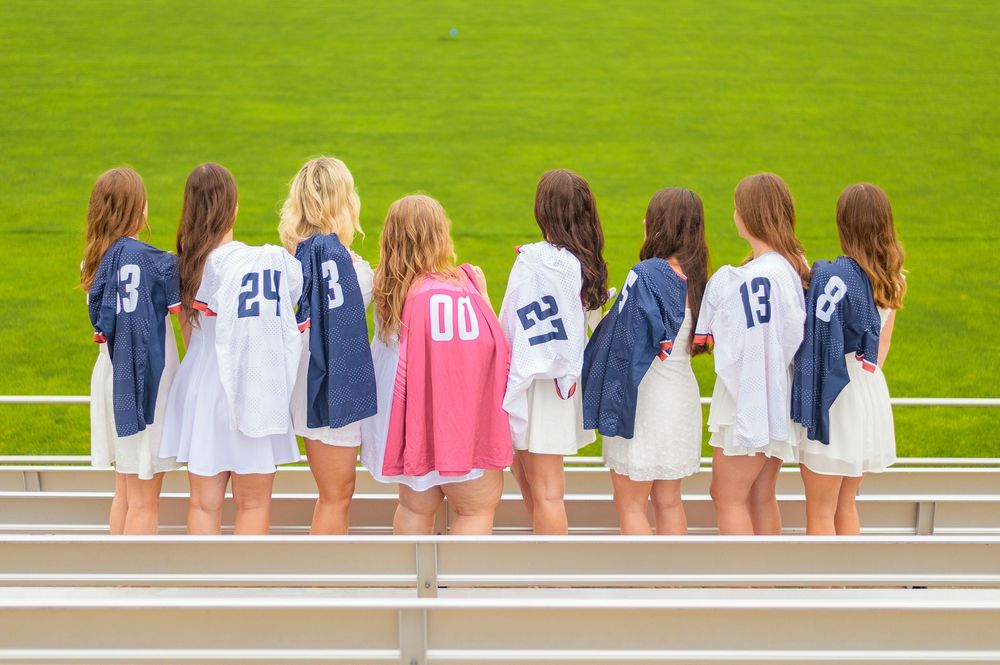 Group photo showing sports jerseys with different numbers on bleachers at athletic field.