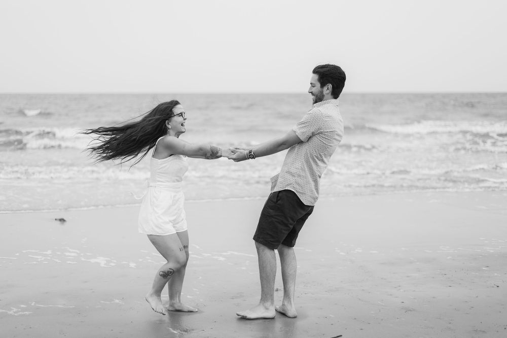 Couple spinning and dancing together on a misty beach shoreline.