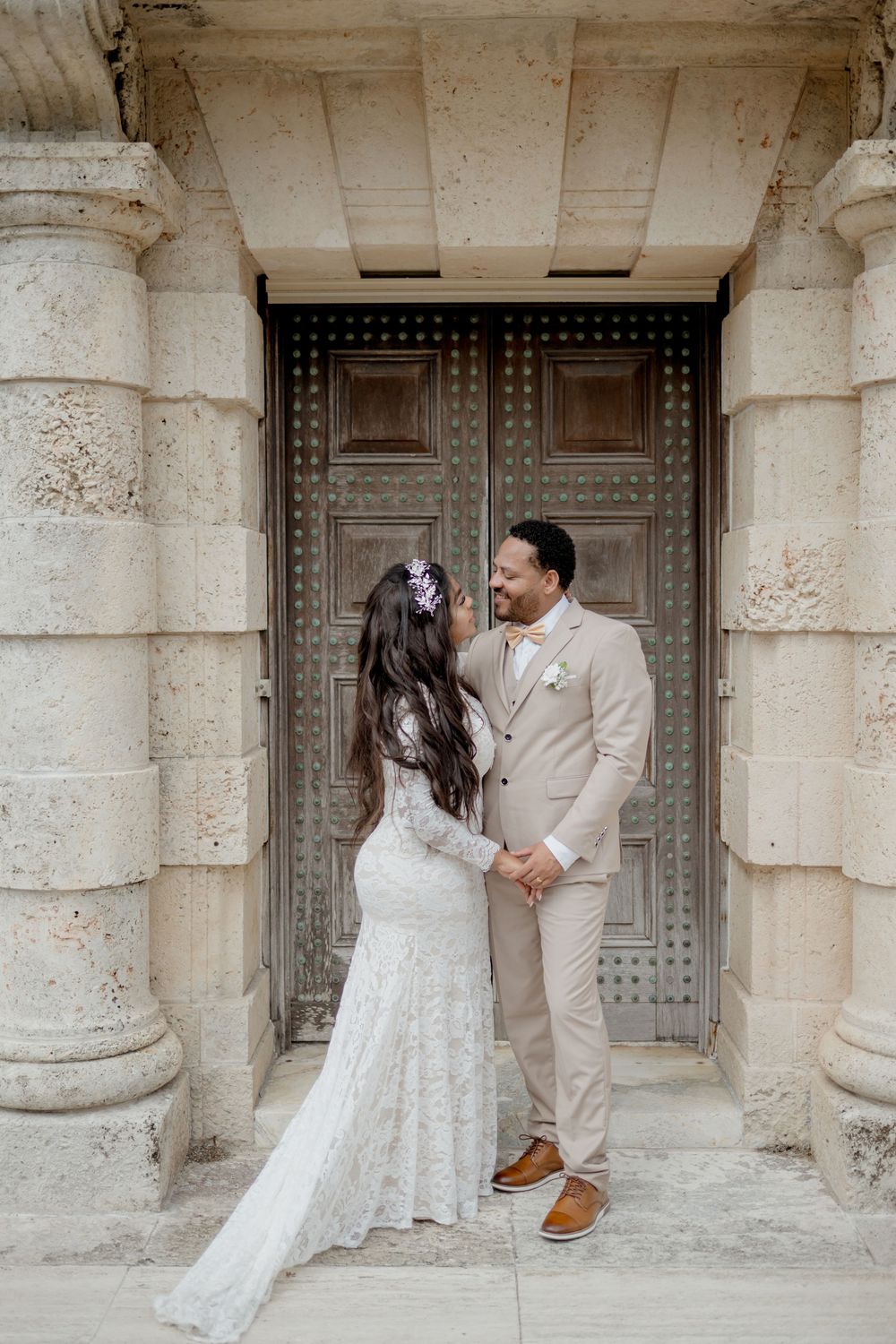 A romantic wedding couple dancing and embracing in front of an elegant stone doorway with ornate architectural details.