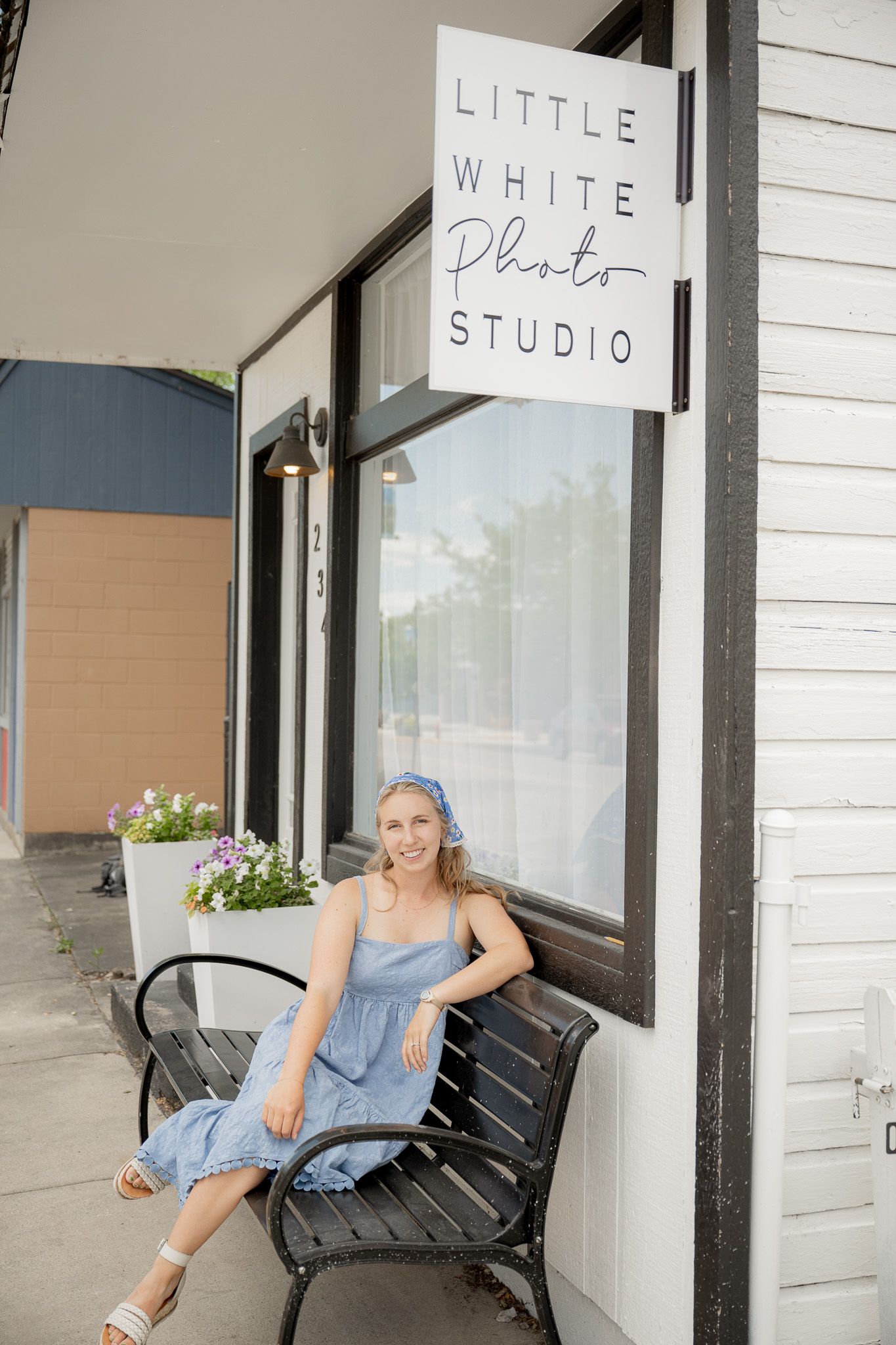 A quaint photography studio storefront with a black bench and 'Little White Photo Studio' sign mounted on white siding.