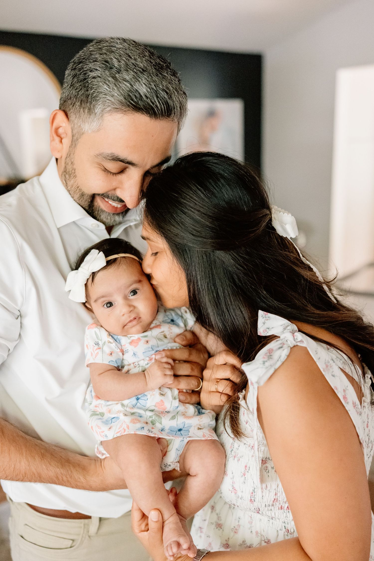 An intimate family moment as loving parents share a tender moment with their baby wearing a floral outfit.