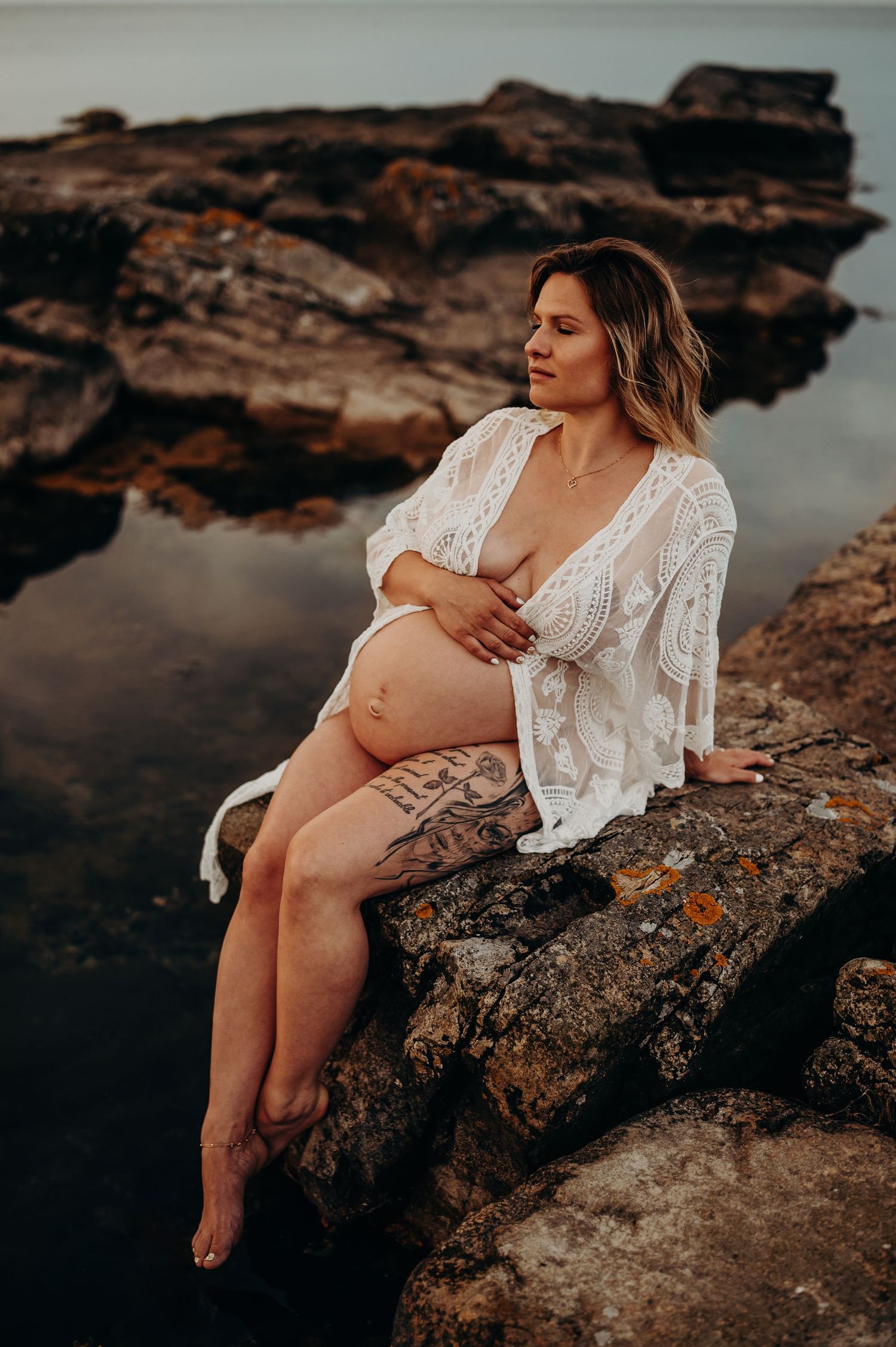 gravid kvinna sittande på en klippa i vattnet iklädd en vit spetskimono