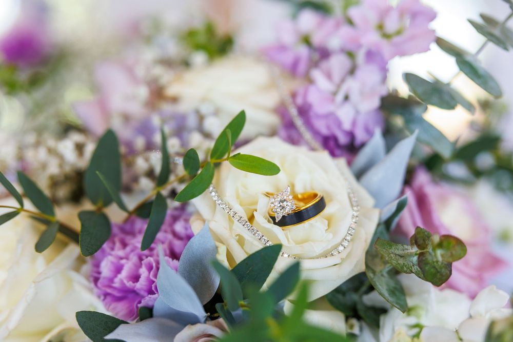Delicate purple and white flowers arranged with greenery in an elegant wedding ceremony setting with scattered rose petals.