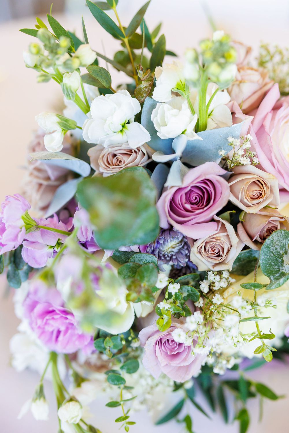 Romantic wedding bouquet featuring pink and mauve roses with mixed greenery and delicate white flowers.
