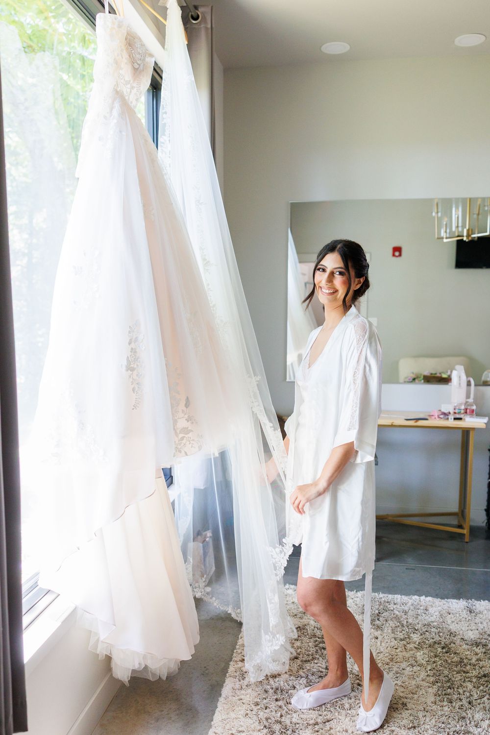 White wedding dresses hanging in a brightly lit room with natural window light.