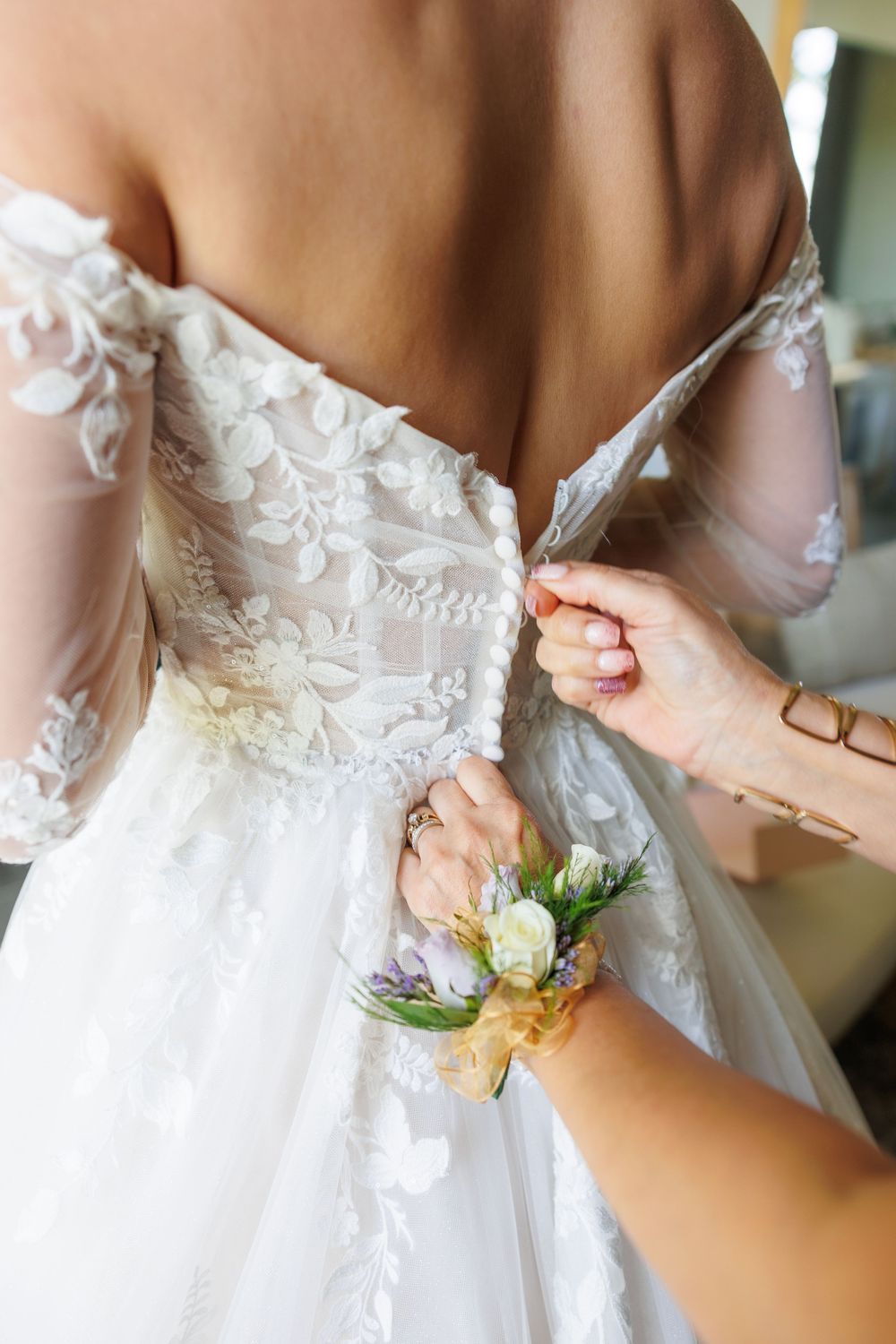 Detailed close-up of hands adjusting delicate lace buttons on a white wedding dress with floral details.