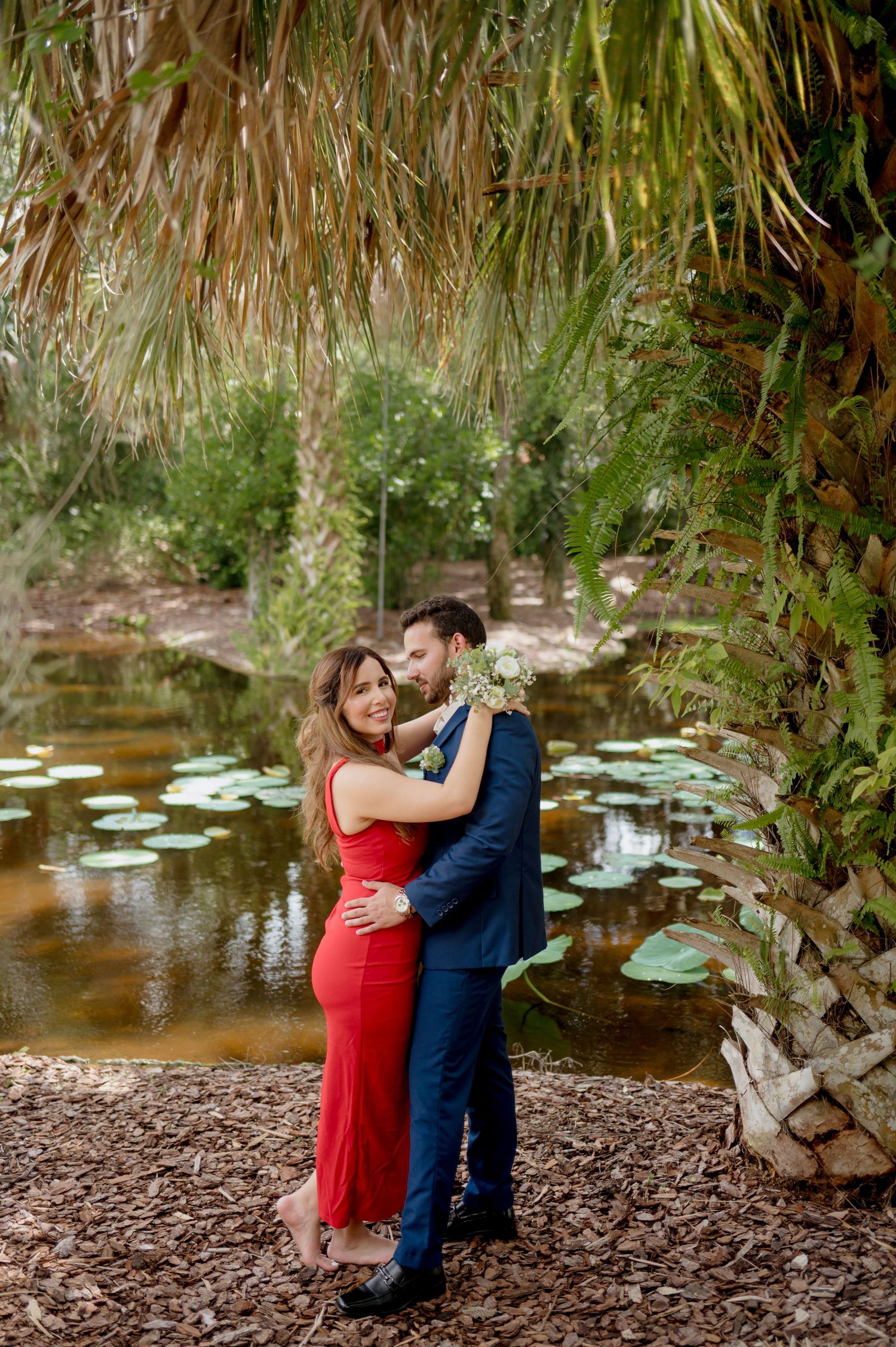 Five sequential photos of a couple in formal attire sharing romantic moments by a tranquil lily pond.