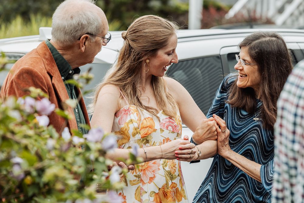 Three people share an animated conversation outdoors near a parked car.