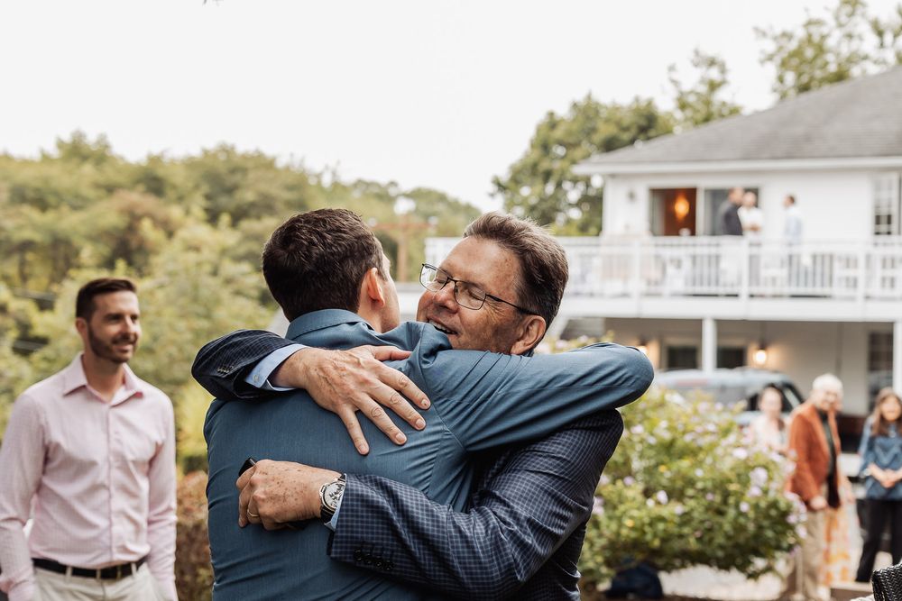 Two people share a warm embrace at an outdoor event with others in the background.