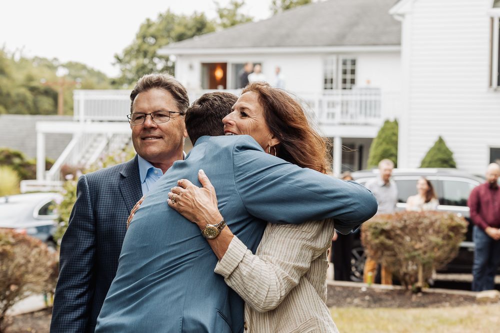 People sharing enthusiastic hugs during an outdoor celebration near a white house.