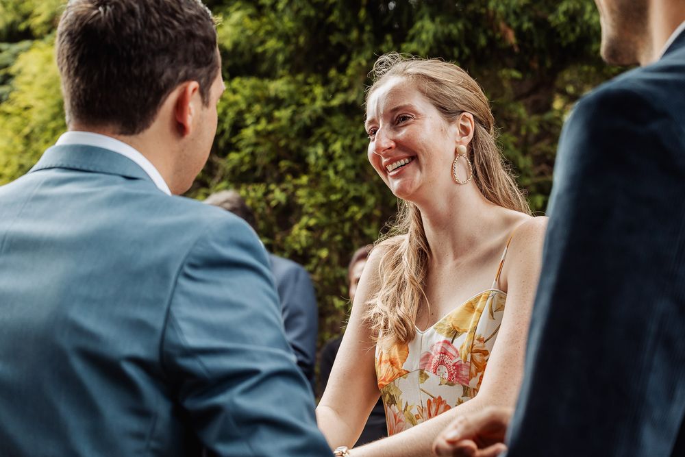 Two people engaged in cheerful conversation outdoors with greenery in background.