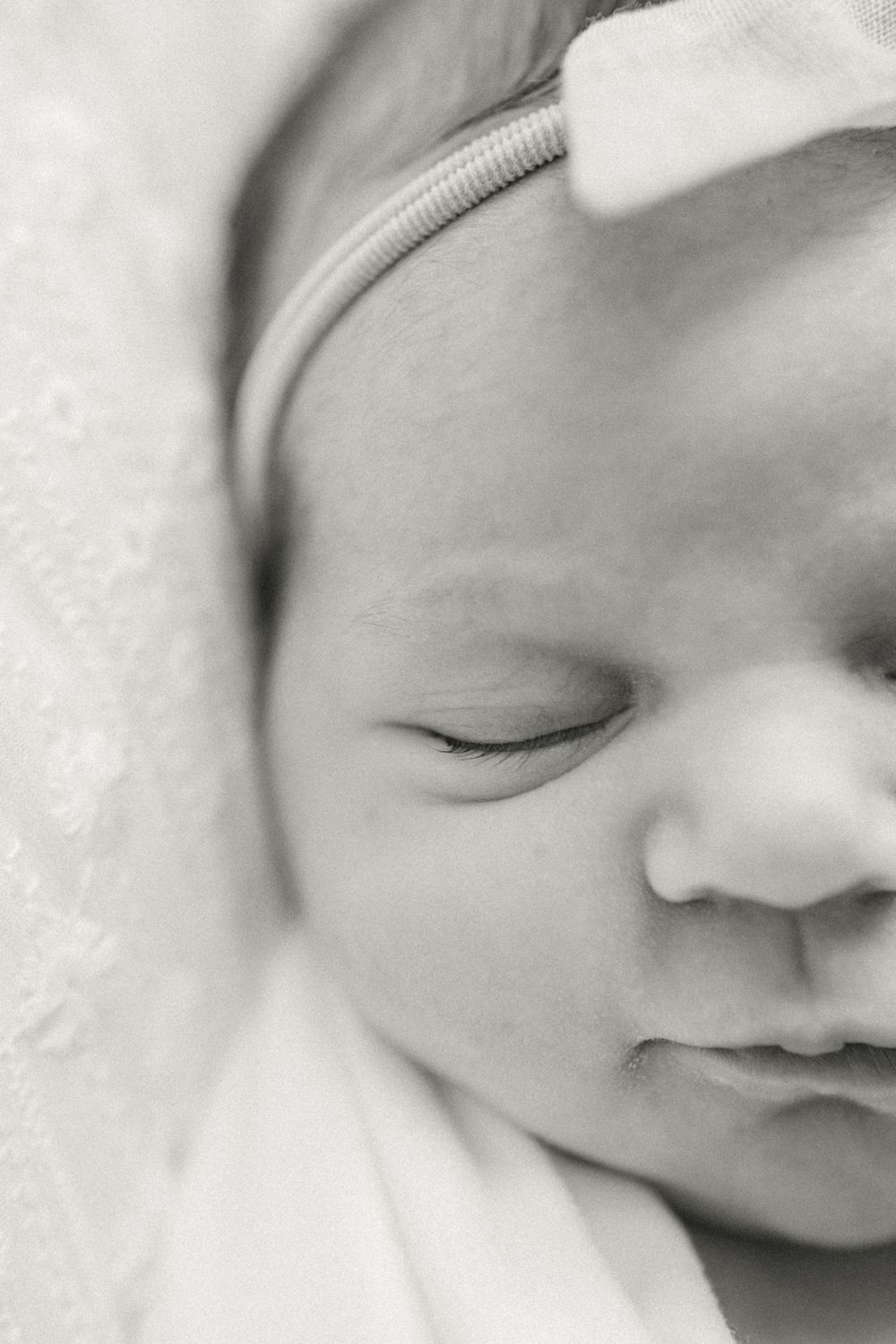 Close-up black and white portrait of a sleeping newborn baby showing peaceful expression in soft lighting.