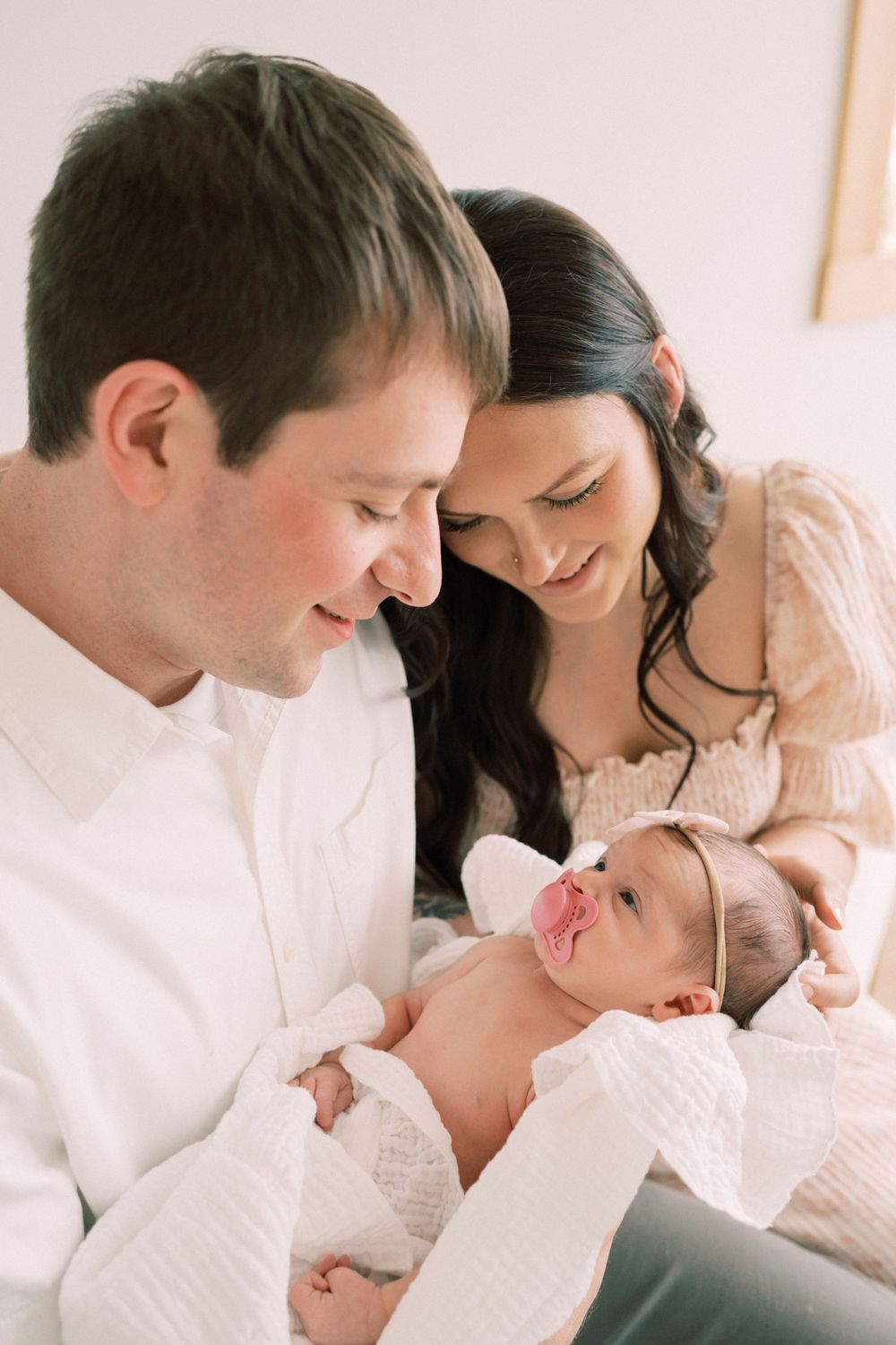 A family shares an intimate moment with their newborn baby, all dressed in soft white and cream colors.