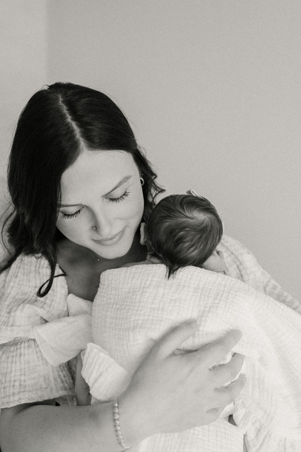 Black and white portrait of a mother in a white textured top holding and gazing lovingly at a swaddled newborn.