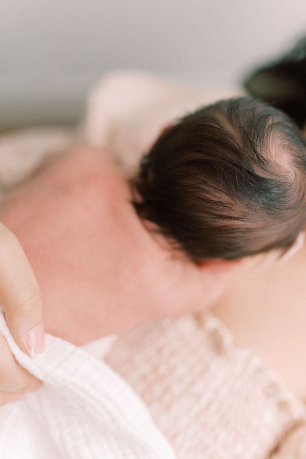 A close-up portrait of dark hair against soft white fabric with a dreamy, gentle aesthetic.