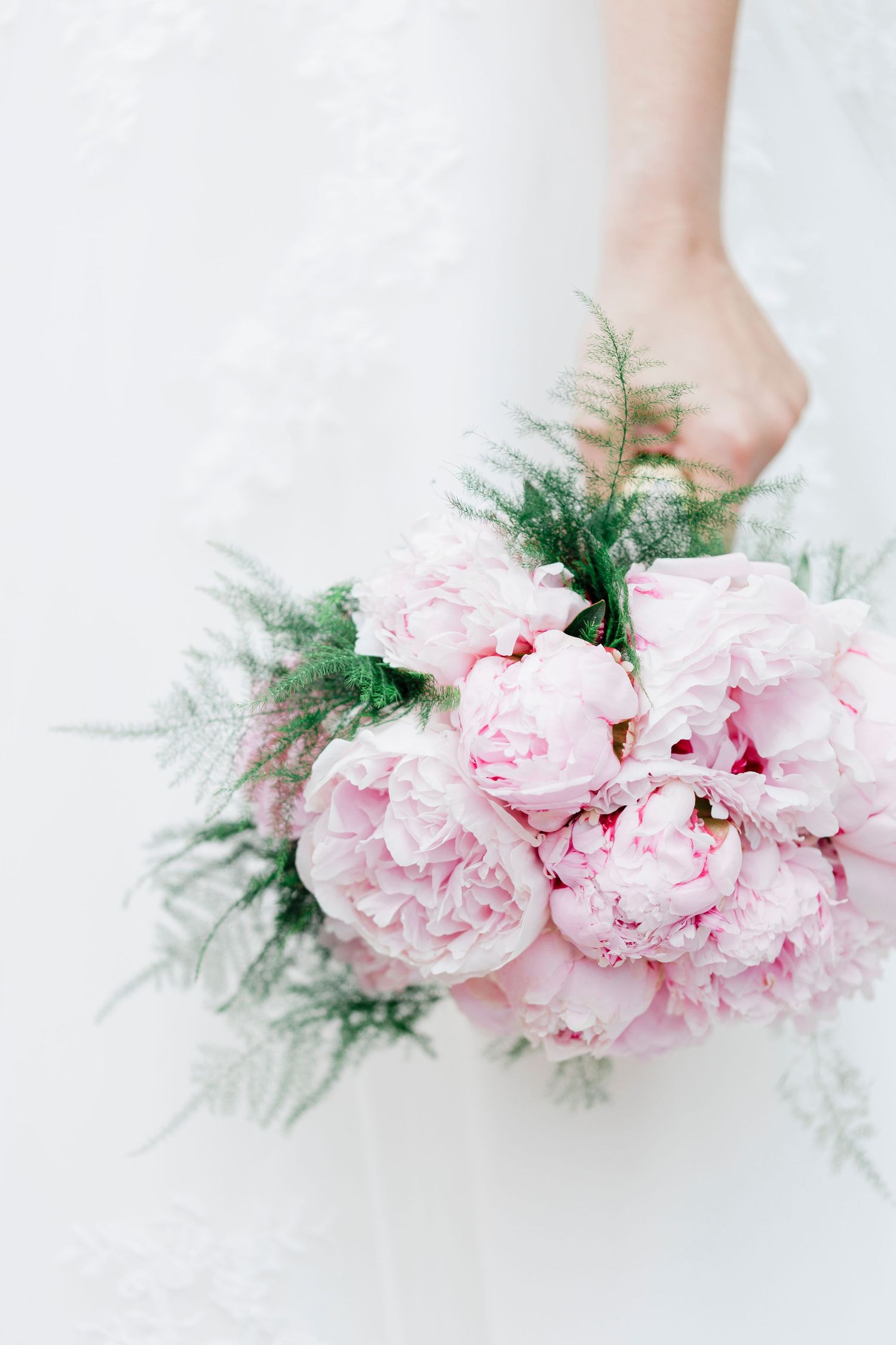Close-up of light pink peonies and greenery in a wedding bouquet.