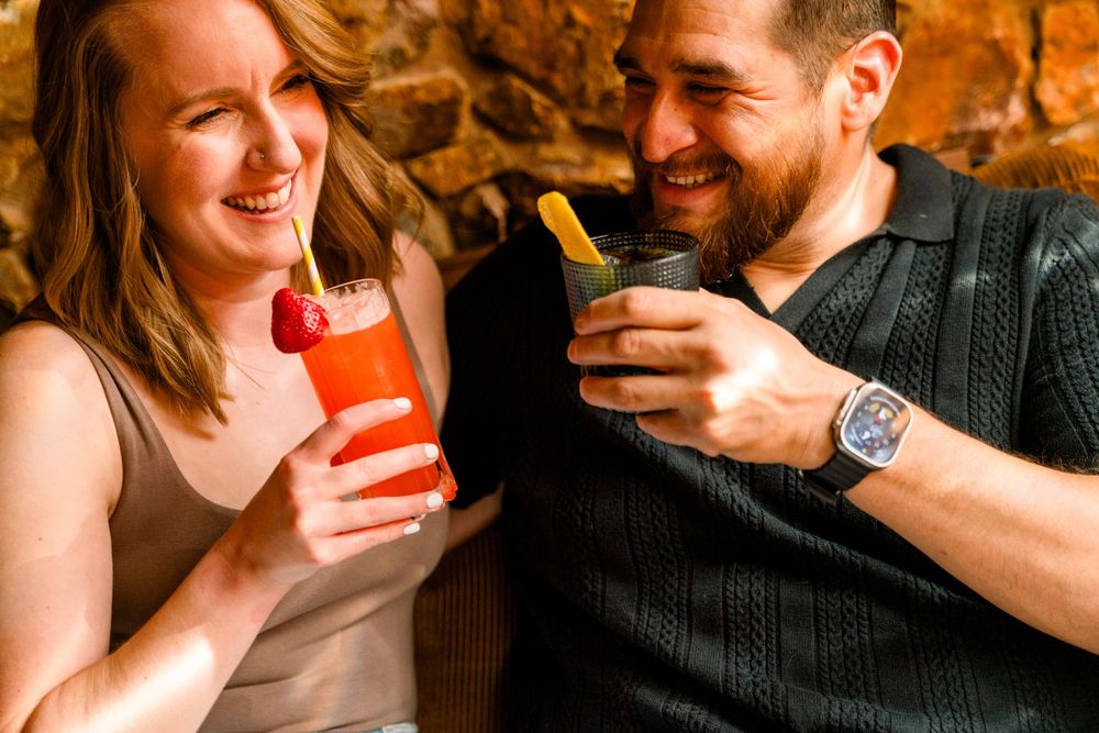 A couple enjoys colorful tropical cocktails while sitting together and sharing a lighthearted moment.