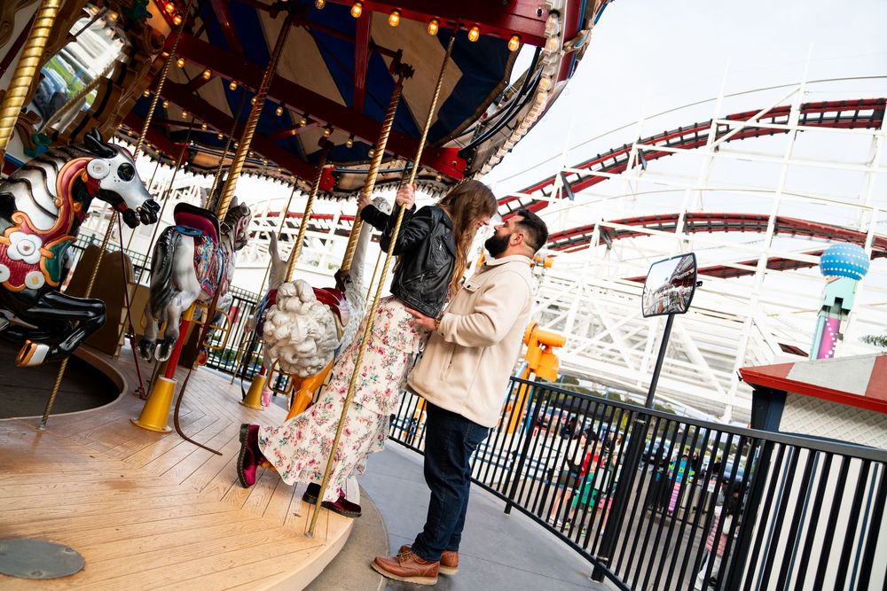 People enjoying a carousel ride at an amusement park with a rollercoaster track visible in the background.