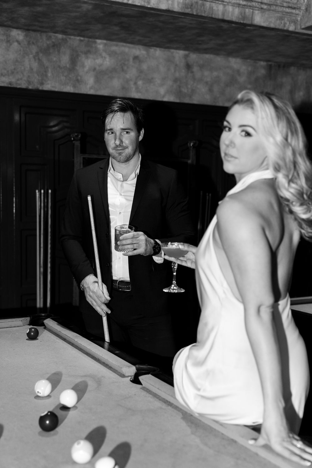 Stylish couple playing pool in formal attire at an elegant venue in black and white photography.