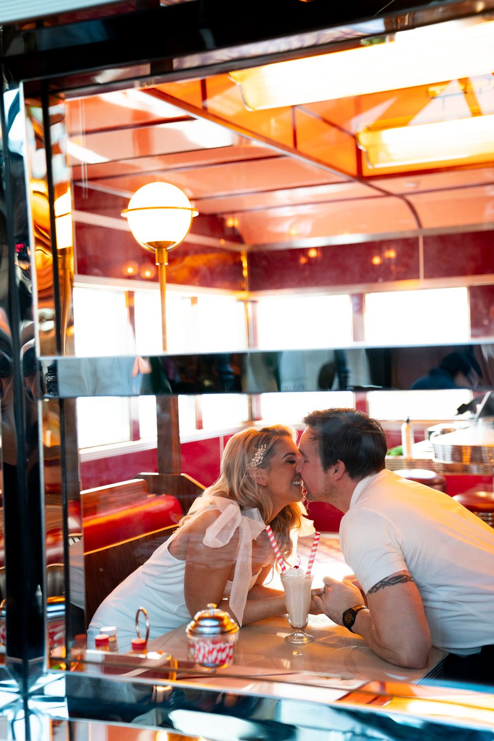 A romantic couple shares an intimate moment together at a retro-style diner booth with red seating and vintage lighting.