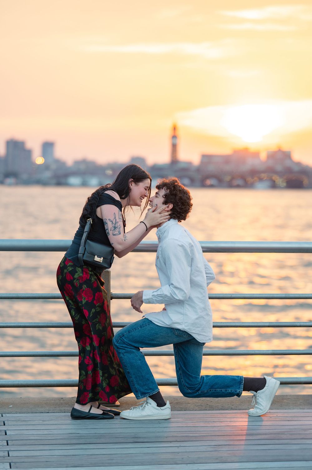 Couple kissing after their proposal at sunset on a waterfront pier with city skyline in NYC at Hudson River Park