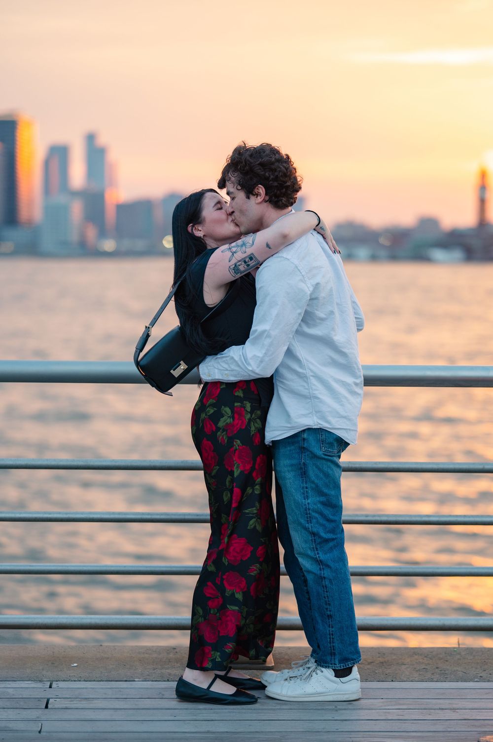 Engaged couple share an intimate moment on a pier during sunset with a city skyline visible in the background after their NYC proposal