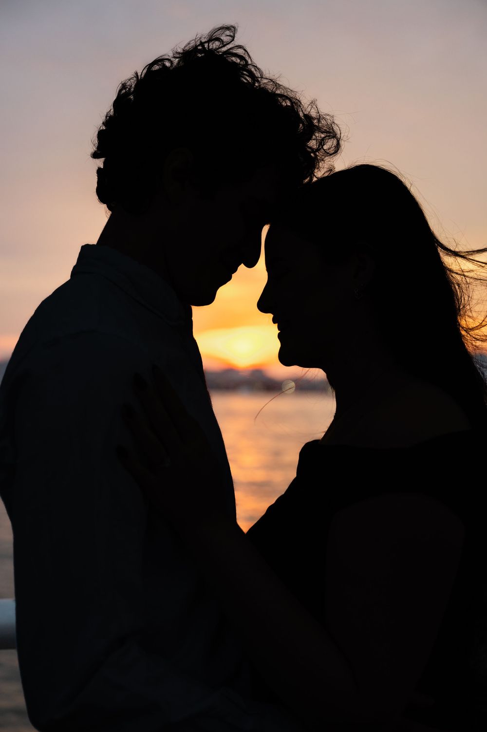 Silhouette of a romantic couple against a golden sunset sky over water, Joliette Marie Photography