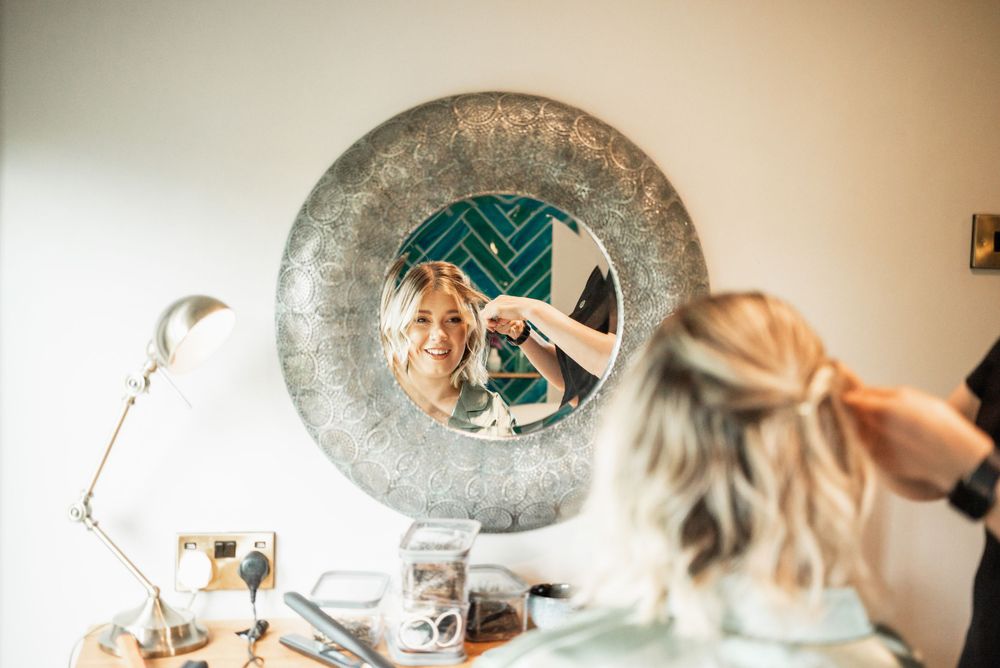 Wedding day hair styling preparation reflected in a round vintage mirror.