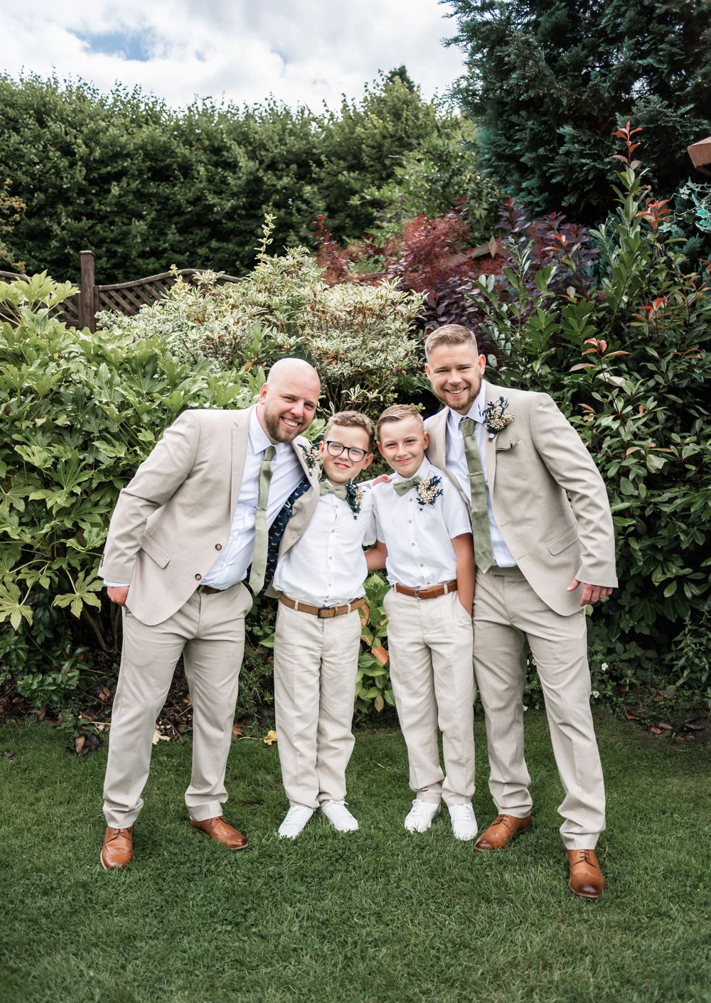 Wedding party in coordinated beige and white attire pose in a garden setting.