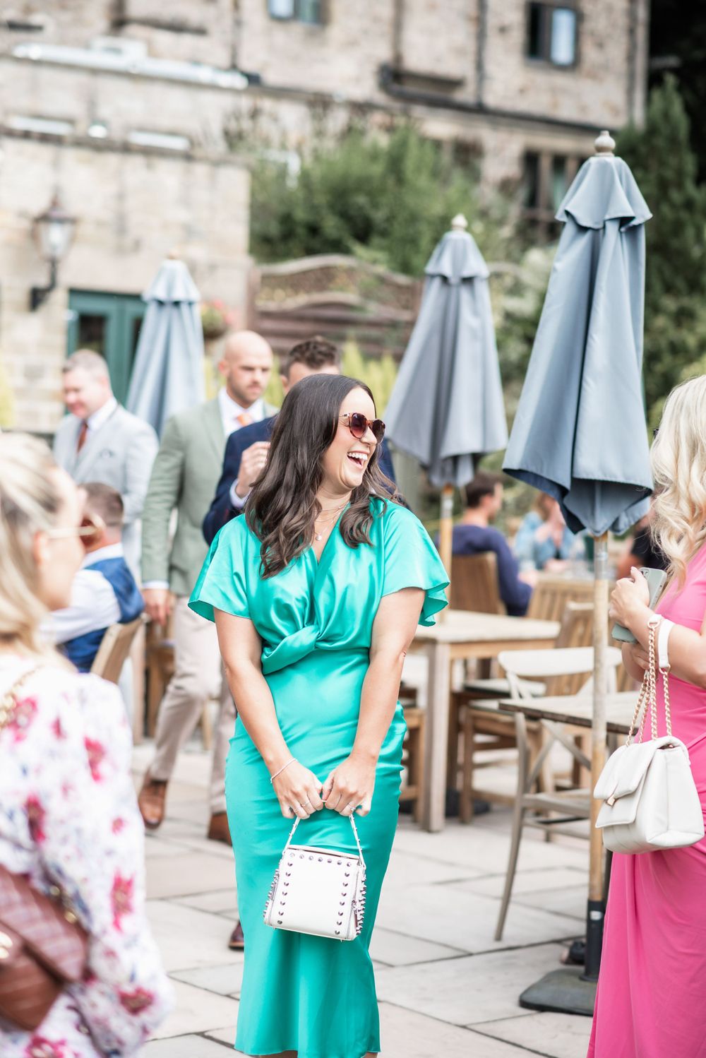 Woman in turquoise dress laughing at outdoor wedding reception with patio umbrellas.