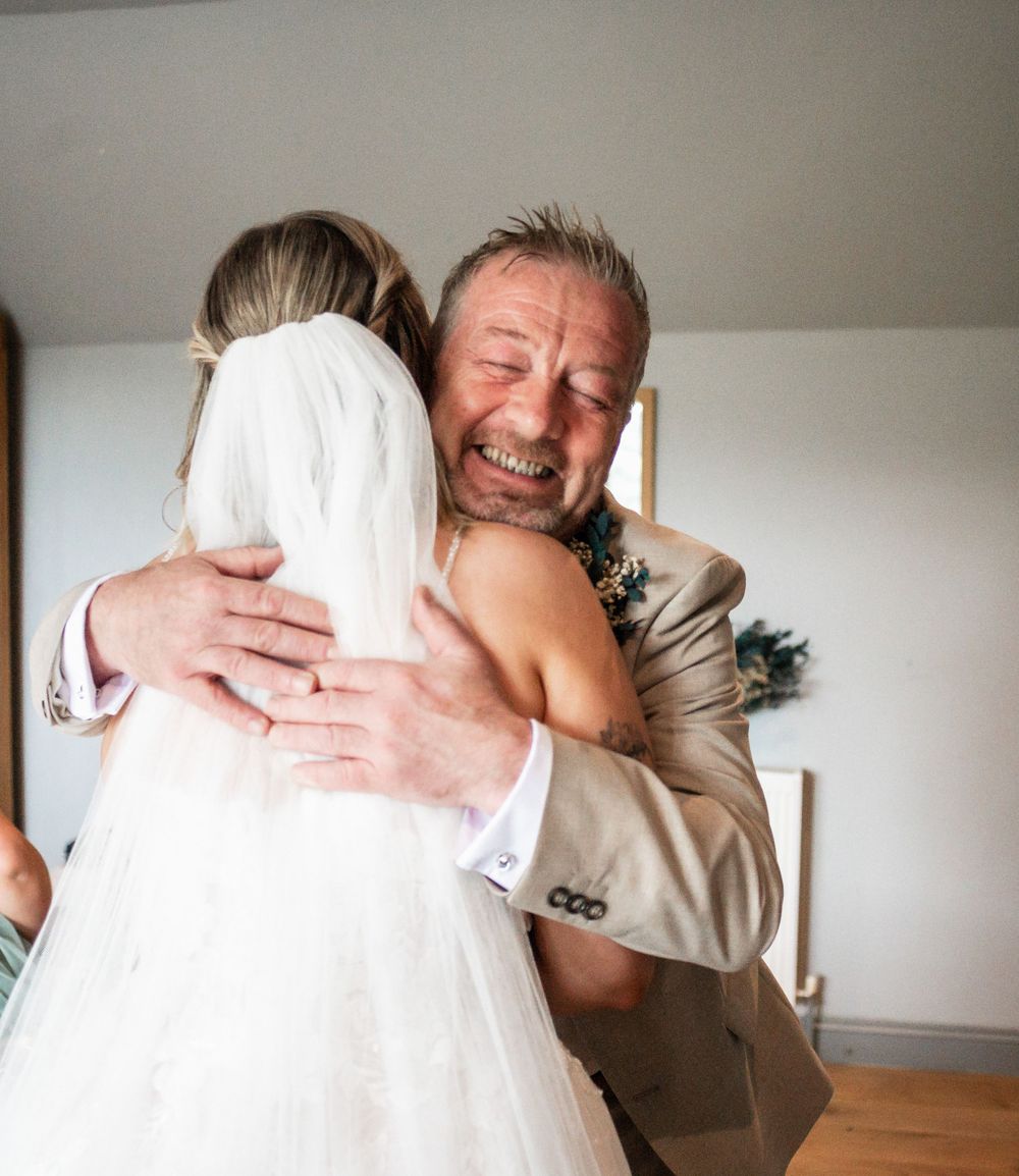 Emotional embrace between two people at a wedding, with one wearing a light colored suit.