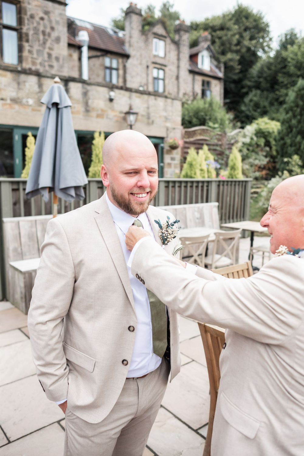 Two people in light beige suits sharing a moment on an outdoor patio of a stone building.