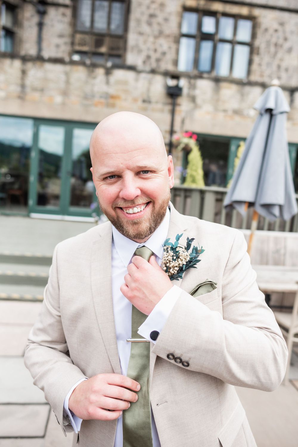 A formal portrait outside a stone building showing a cream suit and boutonniere.