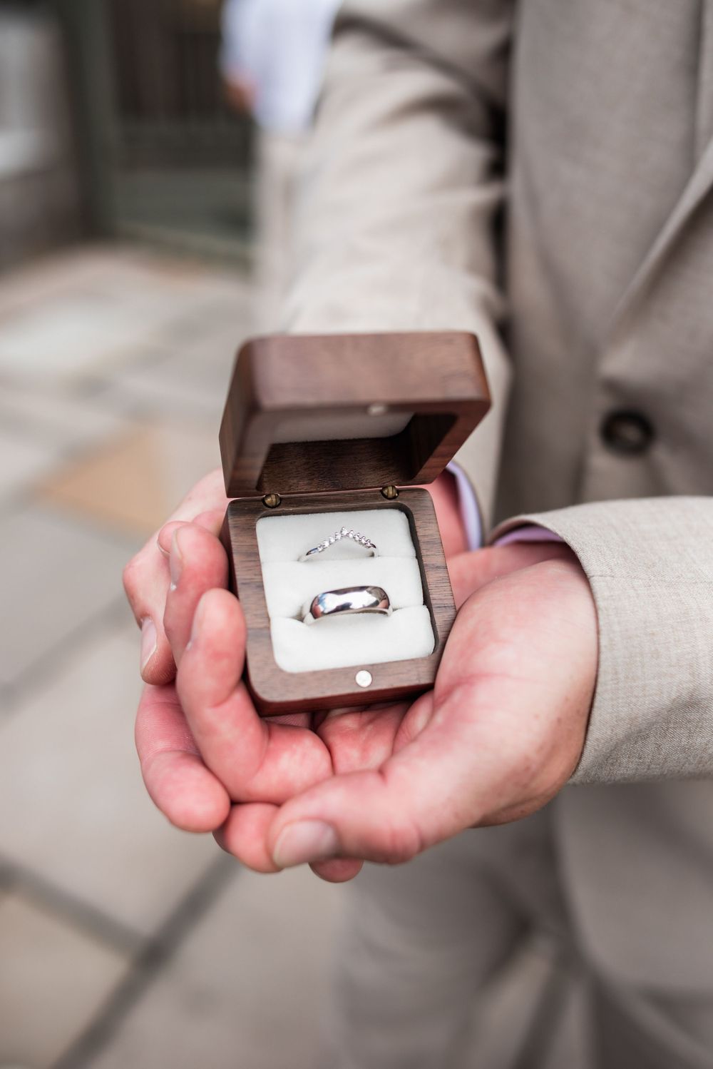 Close-up of hands holding a brown wooden ring box containing wedding bands.