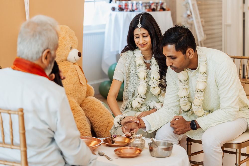 Traditional ceremony with couple in white attire and floral garlands seated at a table with offerings.